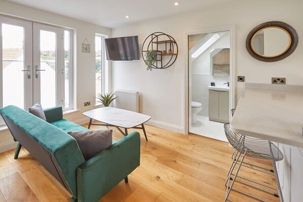 A modern living room with a sofa, a small table, and a TV mounted on the wall.