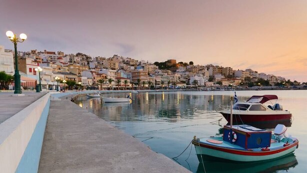 Un muelle con barcos amarrados, un paseo marítimo y edificios al fondo.