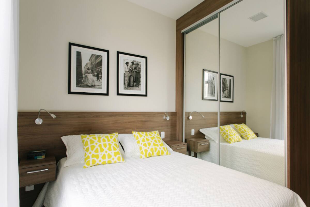 Habitación de hotel con una cama grande, dos mesitas de noche, un tocador, un espejo y dos cuadros en la pared.