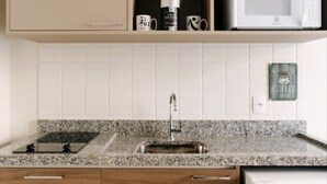 A kitchen with a granite countertop, a stainless steel sink, wooden cabinets, and a built-in microwave. - Jacques Pilon Residence (São Paulo)