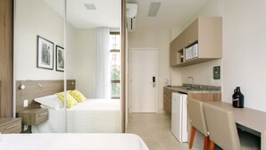 A hotel room with a bed, bedside table, and a view of the kitchen area. - Jacques Pilon Residence (São Paulo)