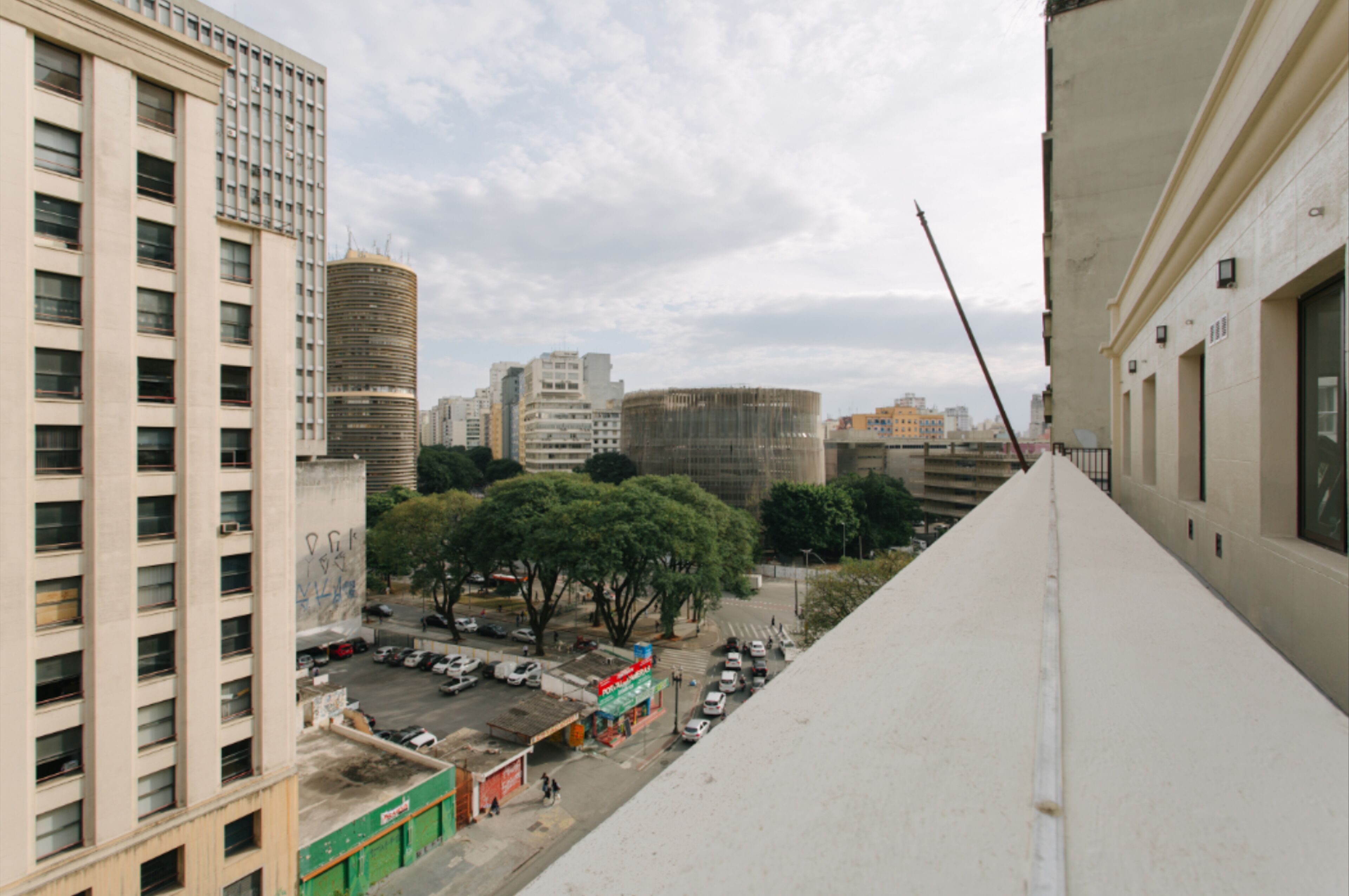 A high-rise building with multiple floors, a parking lot below, and a view of a cityscape with various buildings and trees.