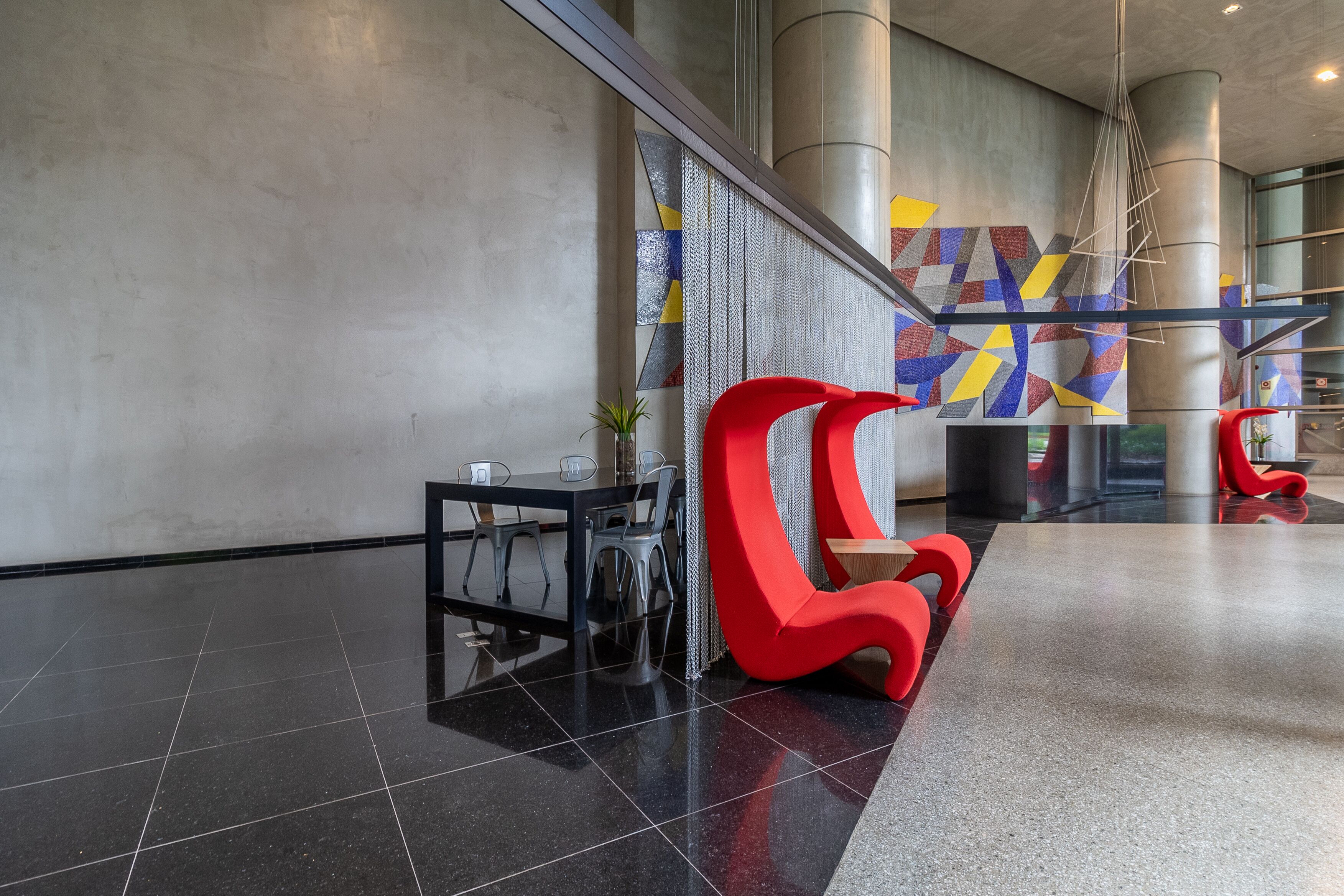 Eine moderne Lobby mit schwarzen Fliesen, einem roten Sessel, einem kleinen Tisch und einer Wand mit geometrischen Mustern.
