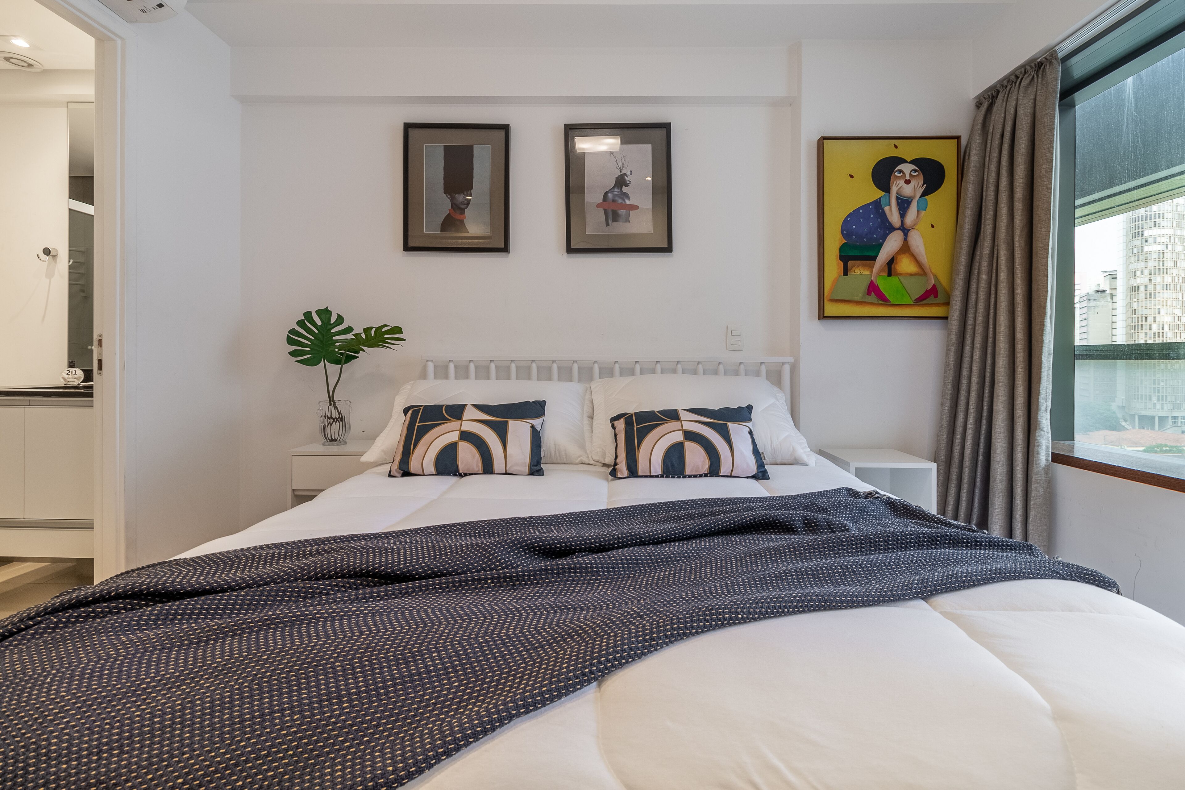 A modern bedroom with a large bed, white bedding, and two framed artworks on the wall.