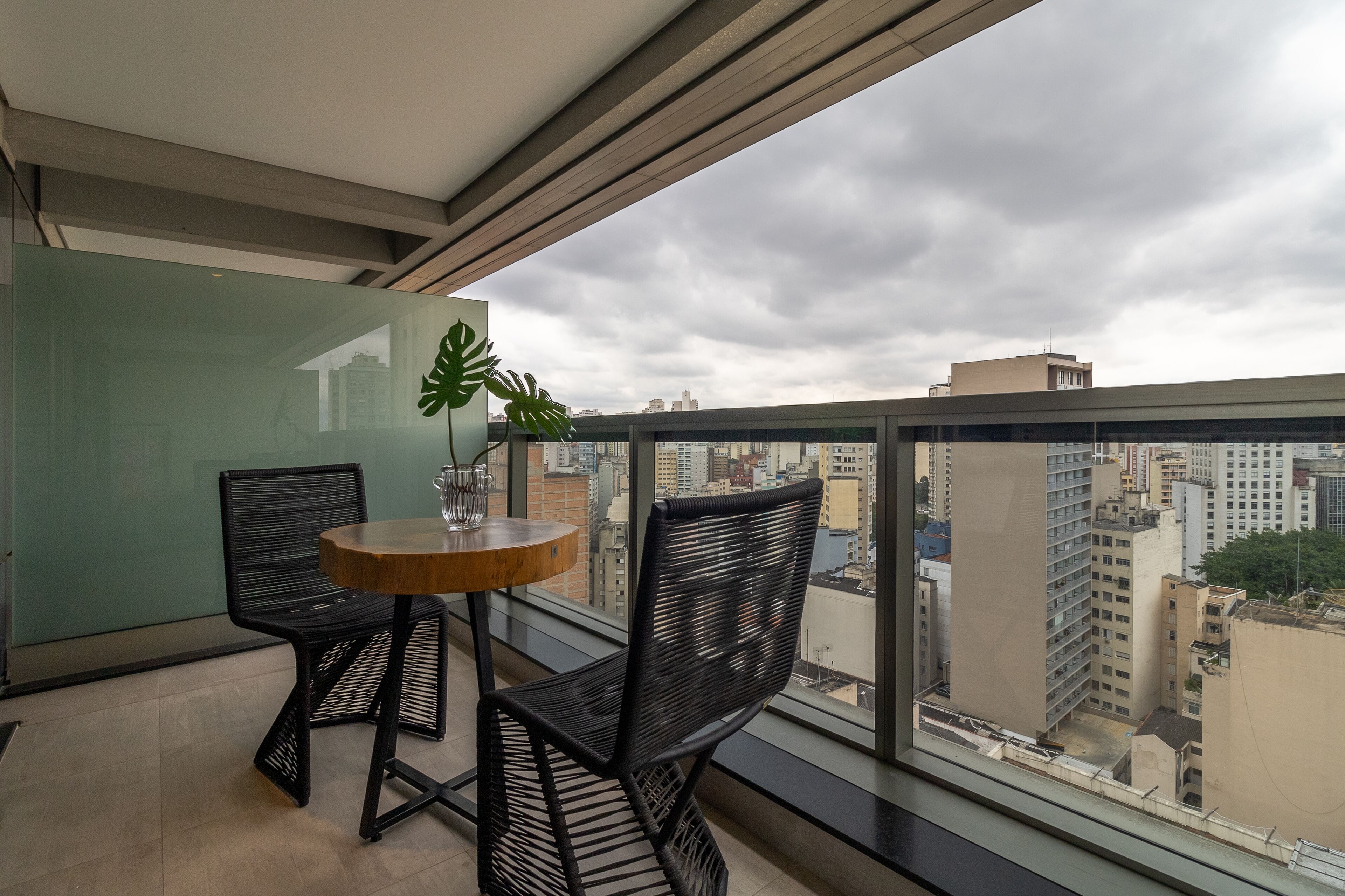 Un balcón con mesa y sillas, una planta en maceta y vistas de la ciudad.
