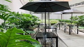 An outdoor patio area with multiple tables and chairs, surrounded by lush green plants.