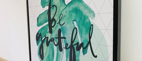 A framed artwork with the phrase "Be grateful" in a stylized font, set against a geometric background.