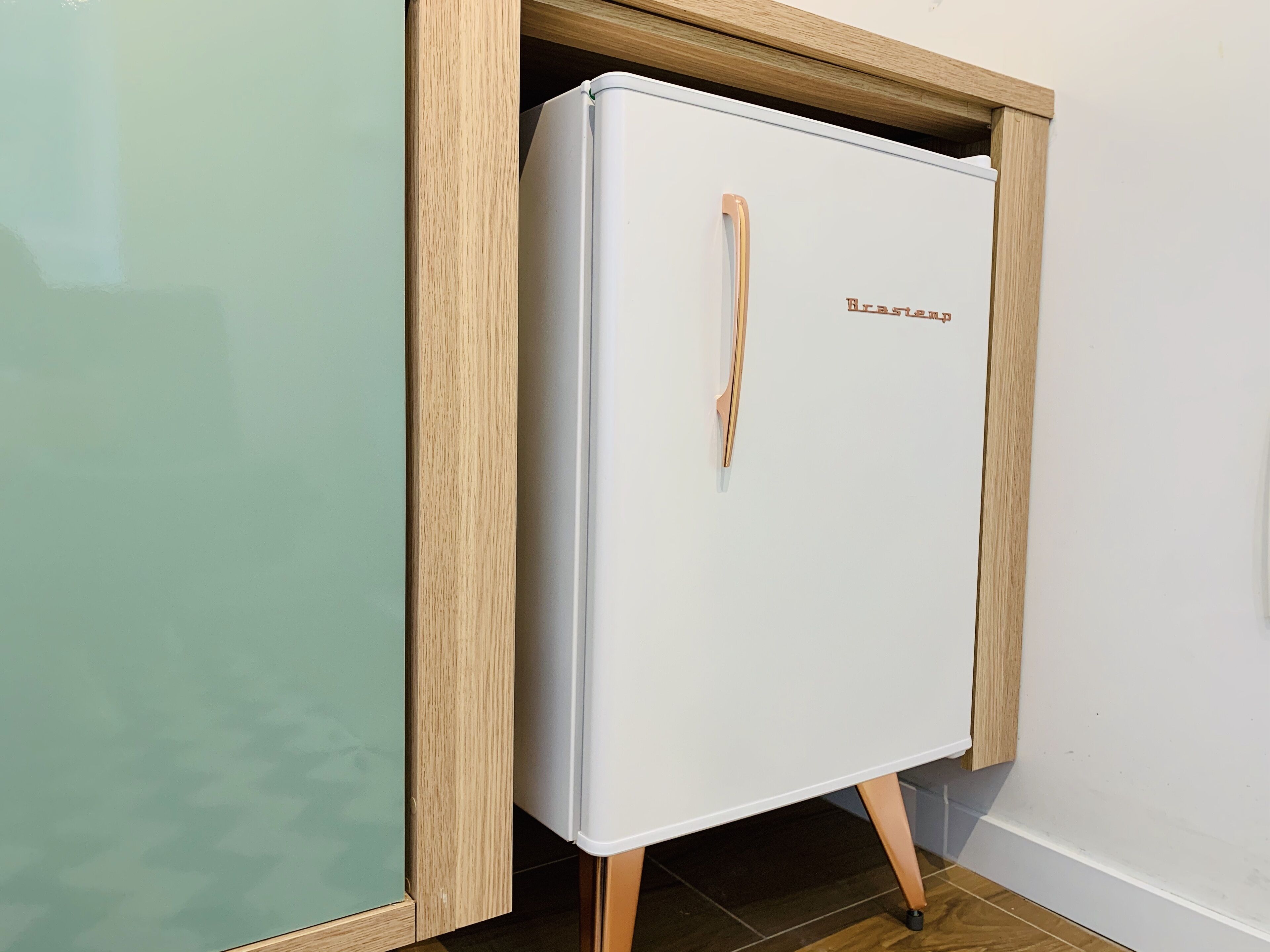 Een witte koelkast met een houten handgreep en de merknaam 'Brilliance' op de deur, geplaatst in een houten kast.