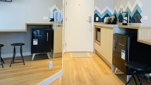 A modern kitchen with a refrigerator, a coffee machine, and a microwave. There are two bar stools and a small table.