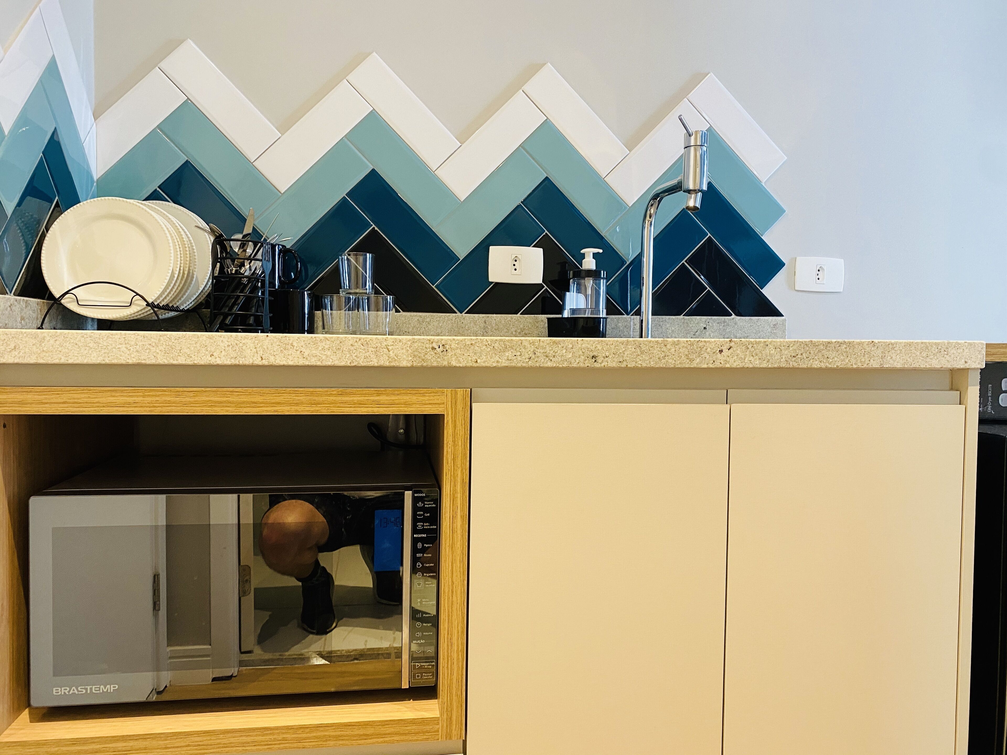 Uma cozinha com micro-ondas em armário de madeira, escorredor de louça com pratos e painel de azulejos.