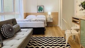 A modern hotel room with a bed, a sofa, a desk, and a nightstand with a lamp.