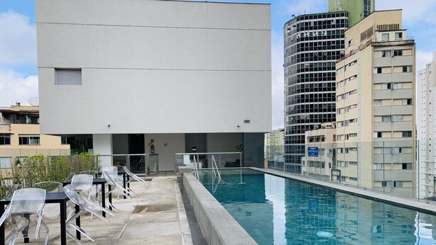 A rooftop pool area with clear glass chairs and a pool, surrounded by modern buildings.