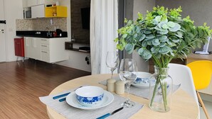 A dining area with a round table set for two, featuring a blue and white floral bowl, two wine glasses, and a vase with green foliage. - Akile Smart Vila Madalena (São Paulo)