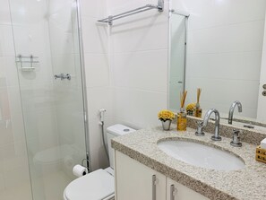 Um banheiro moderno com box de vidro, vaso sanitário branco, pia com bancada de granito e espelho sobre a pia.