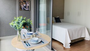 A modern bedroom with a bed, a glass door leading to a balcony, a dining area with a table set for two, and a painting on the wall. - Akile Smart Vila Madalena (São Paulo)