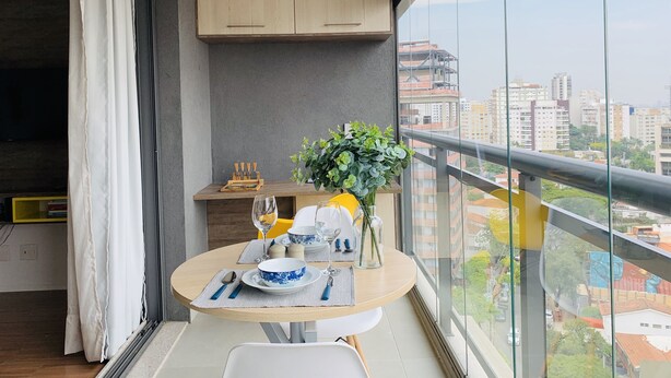 A balcony with a dining table set for two, a small kitchen area, and a view of the cityscape. - Akile Smart Vila Madalena (São Paulo)
