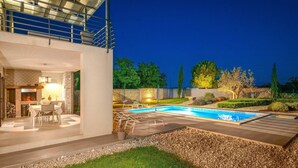 A modern outdoor pool area with a dining setup and a stone wall. - Villa Lounge Kapelana in Istria, Pool, Garden, BBQ (Svetvinčenat)