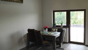 Un coin repas avec une table et des chaises, un tableau accroché au mur et une vue à travers une porte vitrée.
