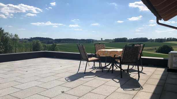 Une terrasse avec une table et des chaises, une vue sur un paysage verdoyant et un ciel dégagé.