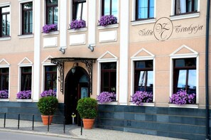 A building with a beige facade, white trim, and purple flowers in window boxes. - Villa Tradycja (Bialystok)