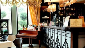 A bar area with a piano, a dining table with chairs, and a view of greenery outside. - Villa Tradycja (Bialystok)
