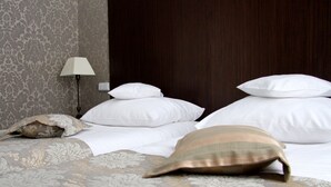 A neatly made bed with white and patterned pillows, a bedside lamp, and a floral-patterned wall. - Villa Tradycja (Bialystok)