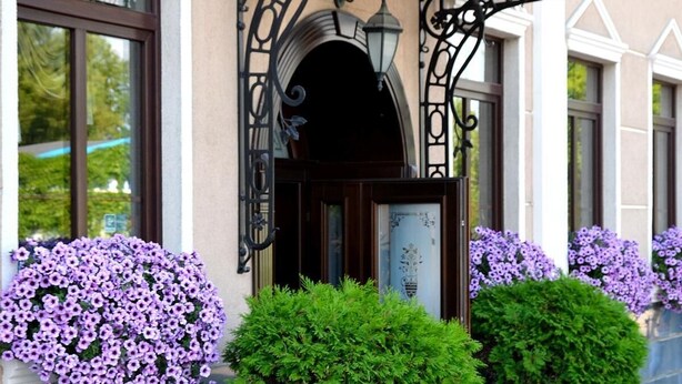A building entrance with a covered entrance, large potted plants, and purple flowers. - Villa Tradycja (Bialystok)