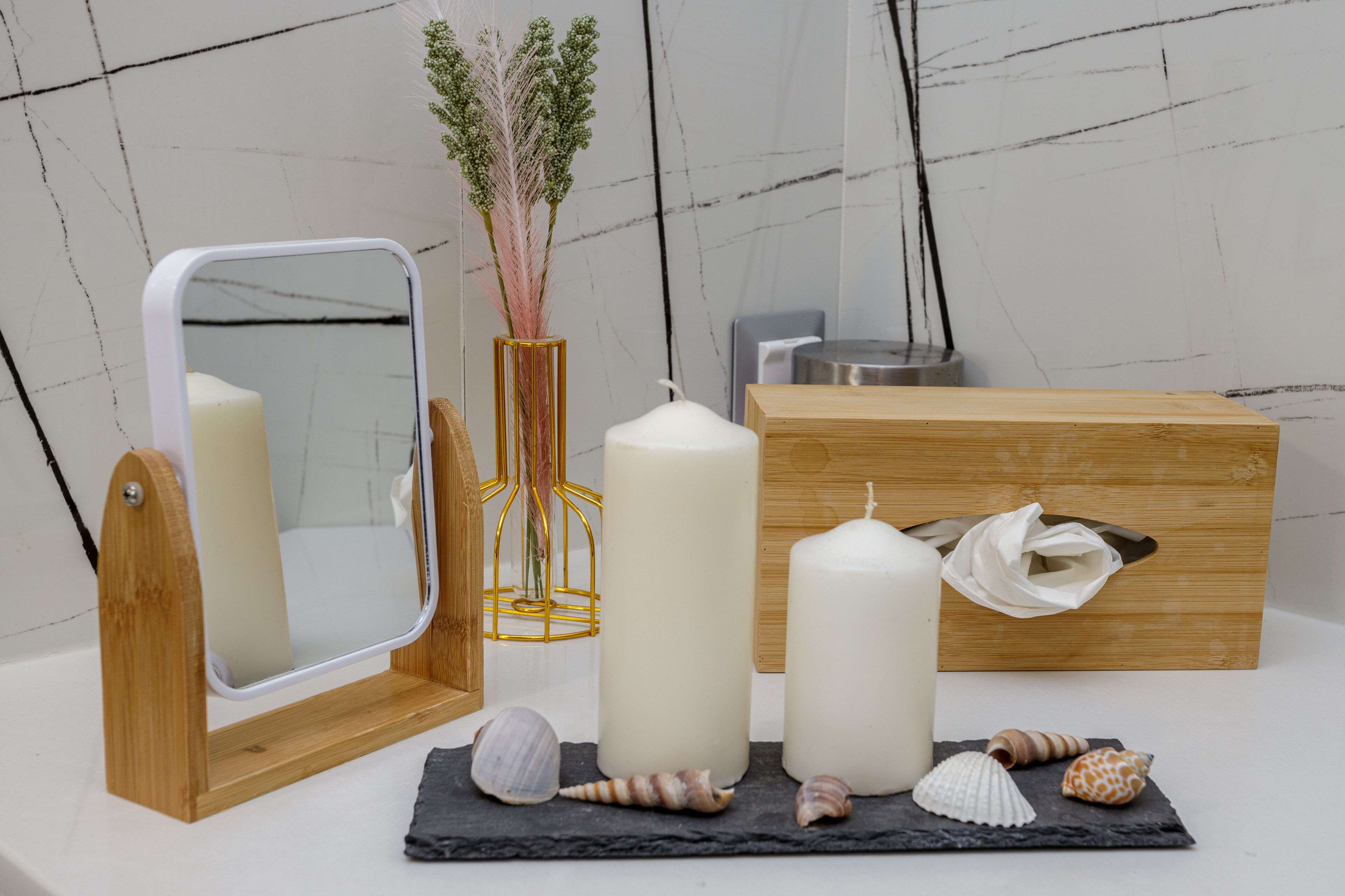 Ein Badezimmer mit Holzwaschtisch, einem Spiegel, zwei Kerzen, einer Papiertauschbox und Meeresschalen auf einer Schiefertablett.