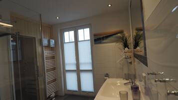 A modern bathroom with a glass shower enclosure, a large sink with a mirror, and a potted plant.