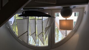 Ett rum med ett runt takfönster, en hängande lampa och utsikt över en byggnad utanför.