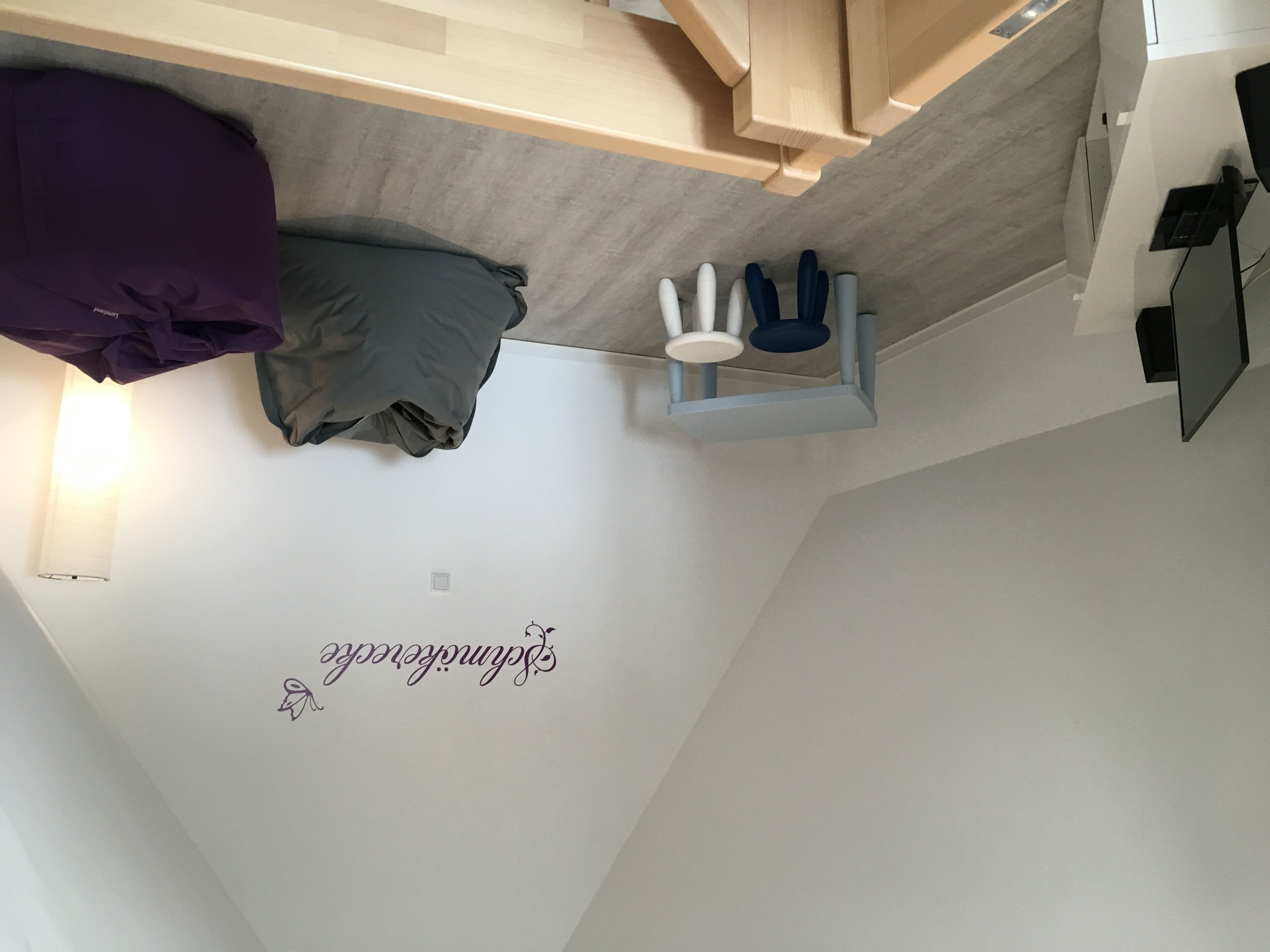 Un dormitorio con cama, mesita de noche, lámpara y estante en la pared.