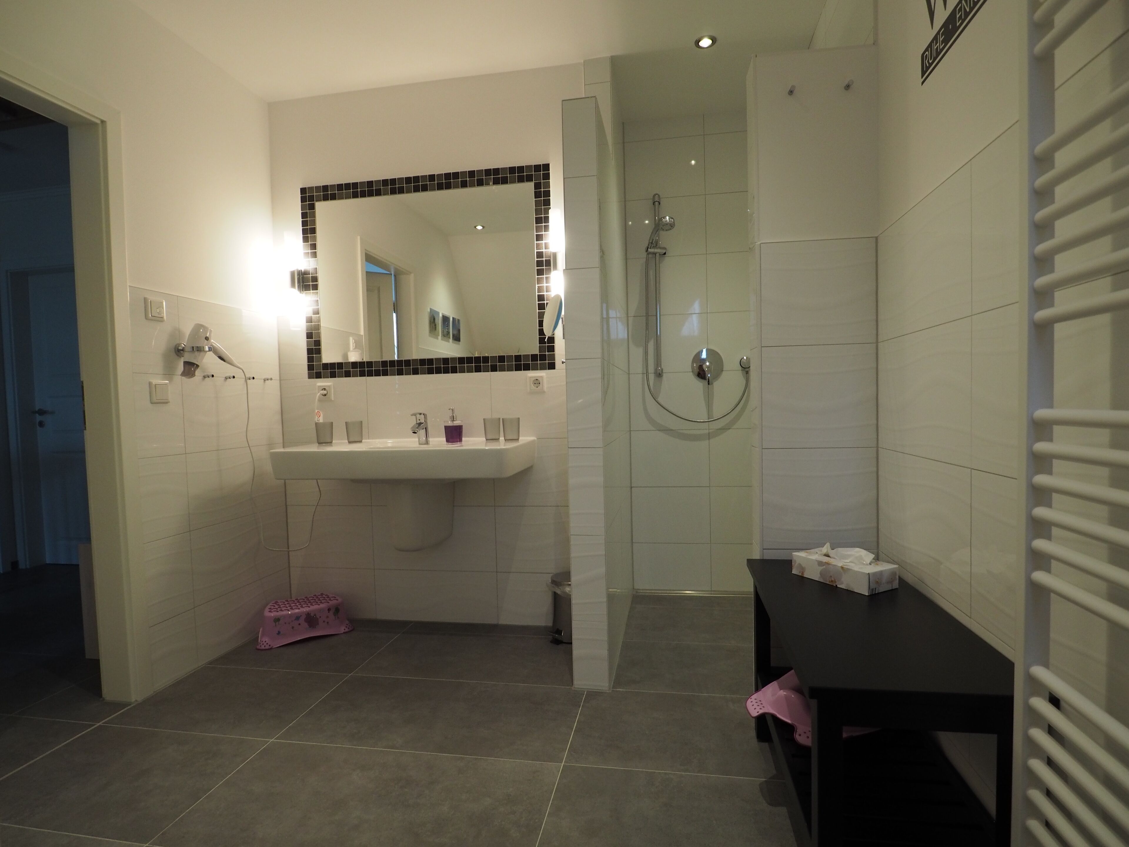 Une salle de bain équipée d’un lavabo, d’un miroir, d’une douche et d’un banc.