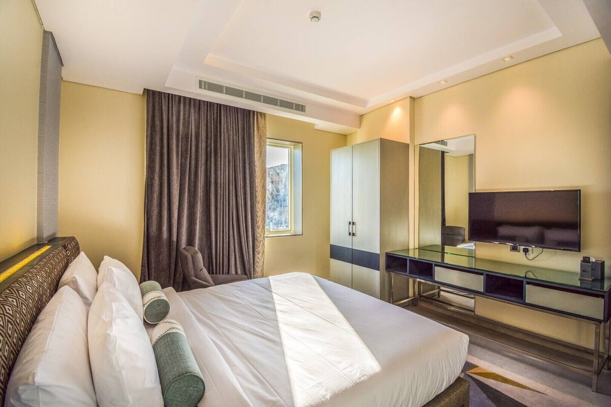 A hotel room with a bed, a desk with a TV, a wardrobe, and a window with curtains.