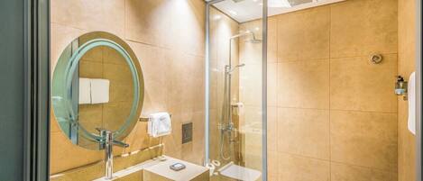A modern bathroom with a glass-enclosed shower, a round mirror, and a beige-tiled vanity.