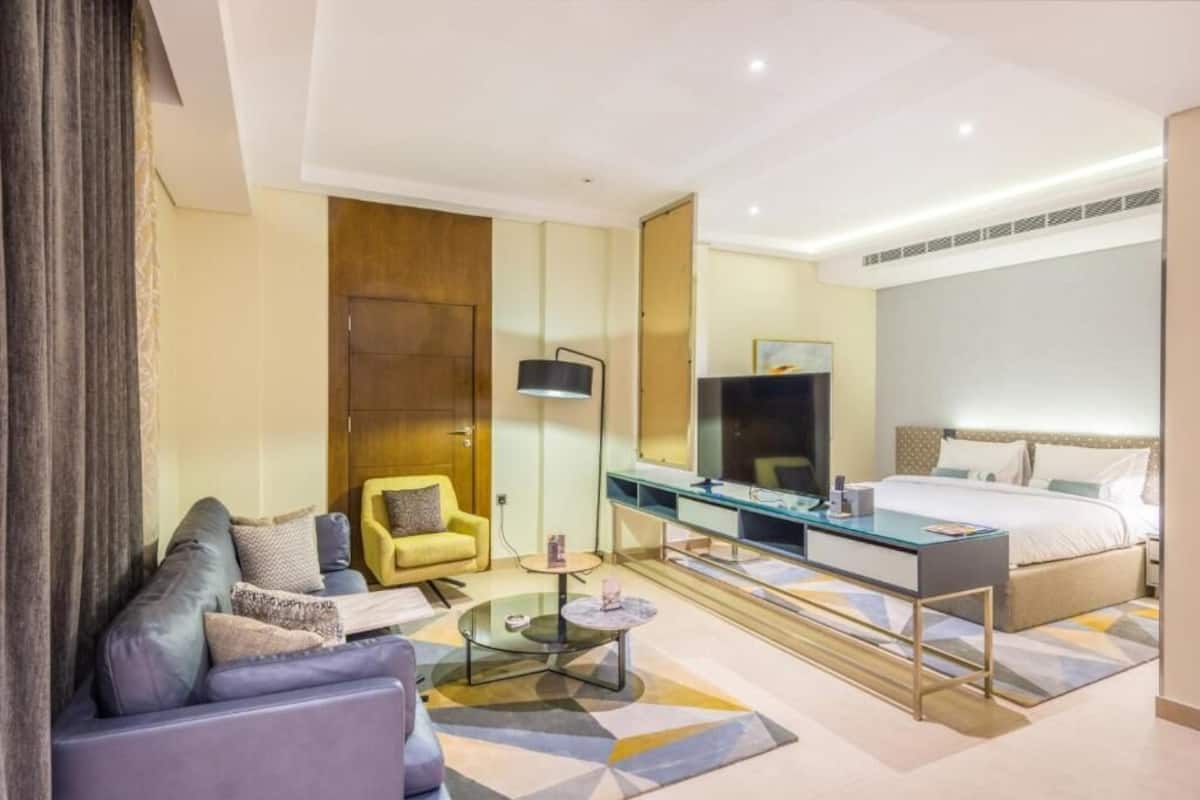 A modern hotel room with a sofa, a desk, a bed, and a TV.