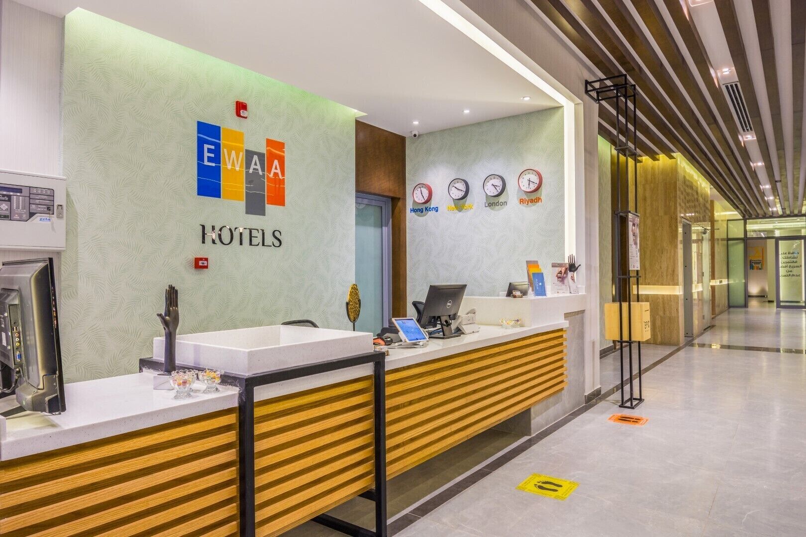 A hotel reception area with a modern design, featuring a reception desk, a digital display, and a wall with clocks showing different cities.