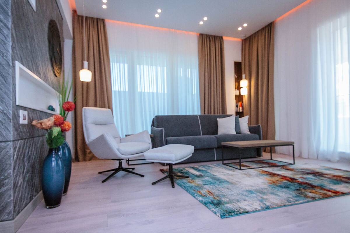 A modern living room with a grey sofa, white armchairs, a coffee table, and a colorful rug.