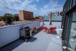 A rooftop terrace with a barbecue grill, red chairs, and a table. - No 6 Apartments (Constanta)