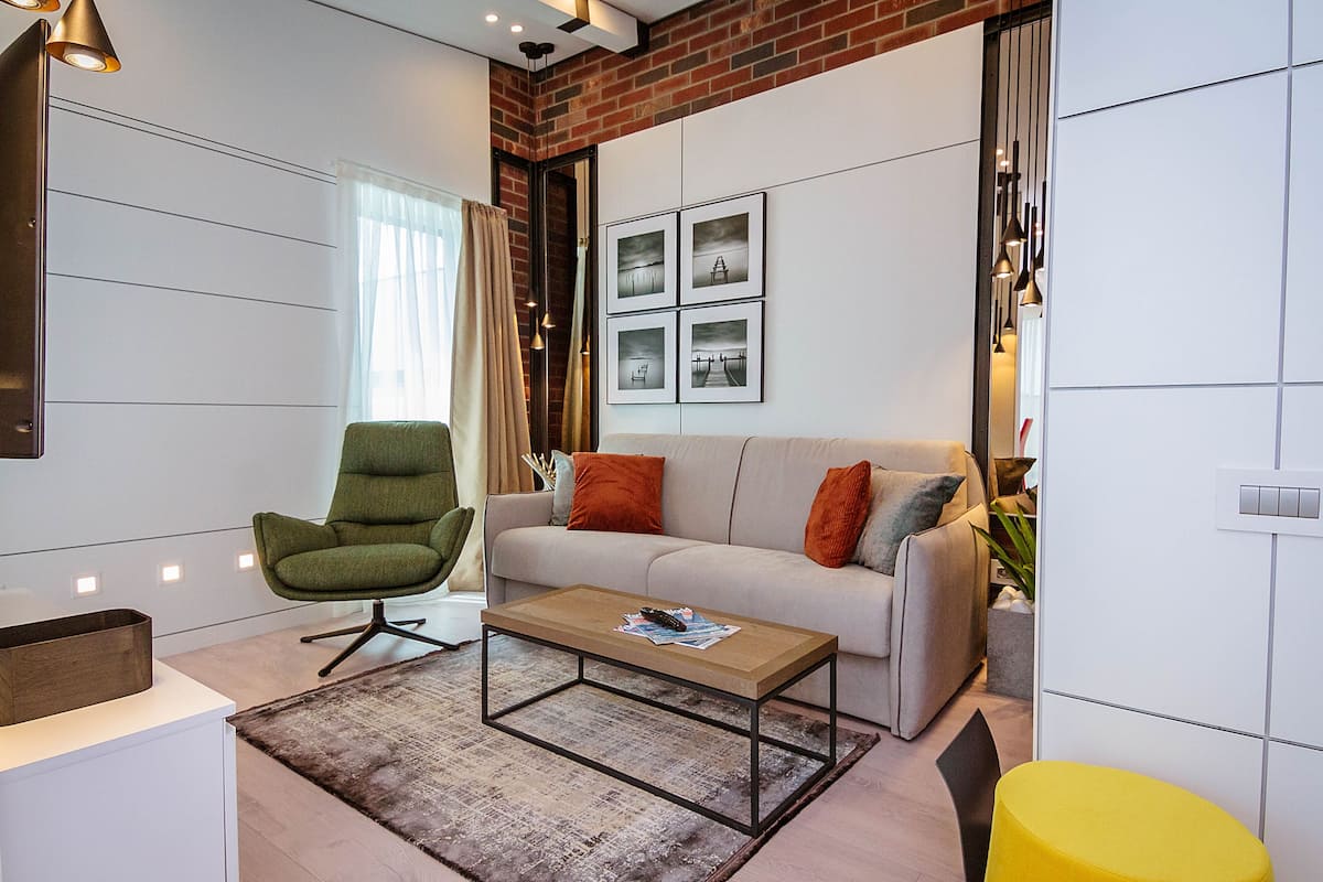 A modern living room with a sofa, a green chair, a coffee table, and a yellow ottoman.