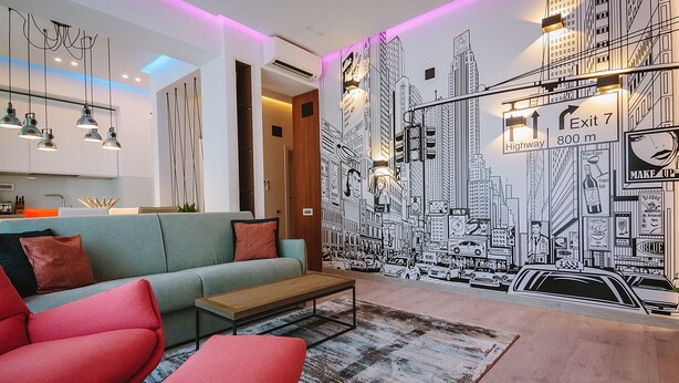 Una sala de estar moderna con un mural de un paisaje urbano, un sofá, una mesa de centro e iluminación colgante.