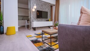 Una sala de estar moderna con un televisor de pantalla plana montado en una pared de mármol, una consola blanca, un reposapiés amarillo y una alfombra colorida.