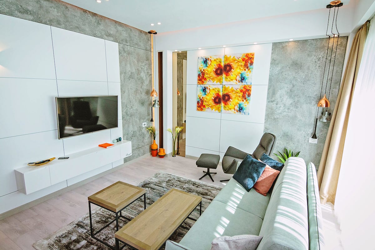 A modern living room with a flat-screen TV, a sofa, two wooden coffee tables, and a large abstract painting on the wall.