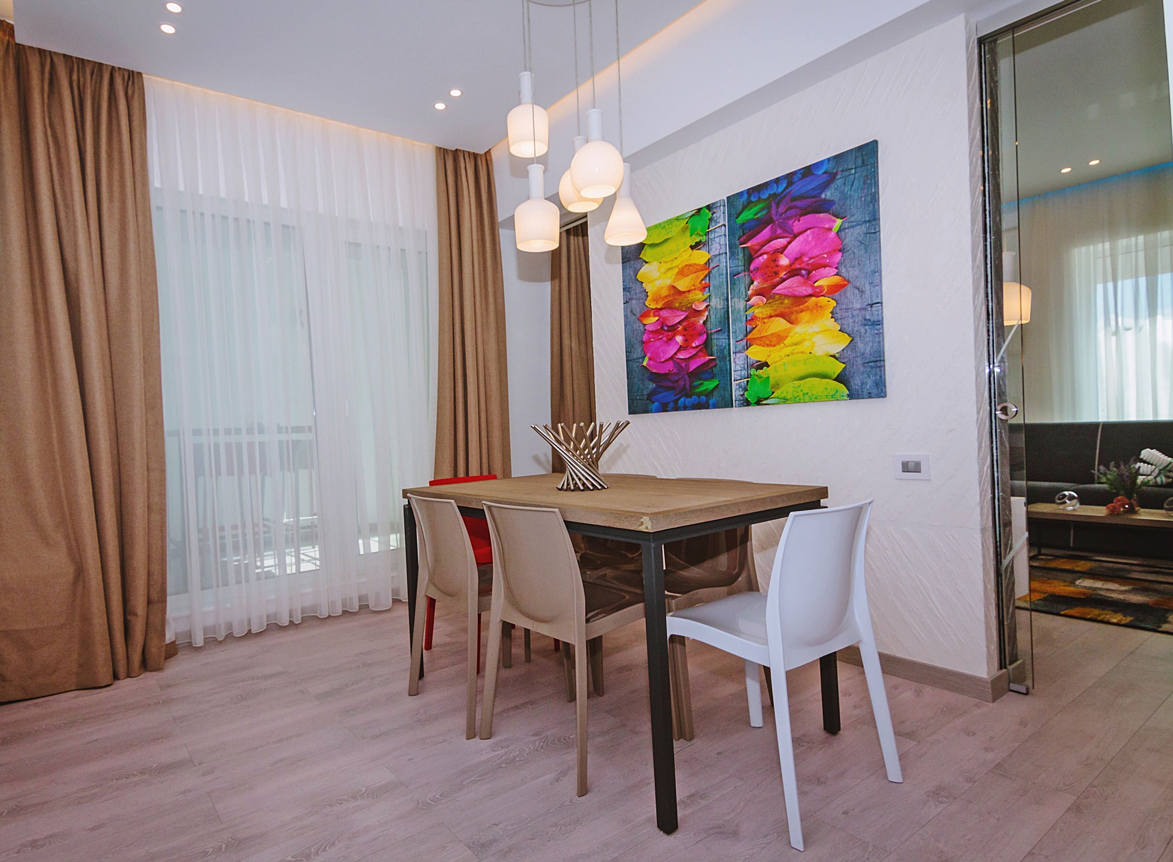 A dining area with a wooden table, white chairs, and a colorful abstract painting on the wall.