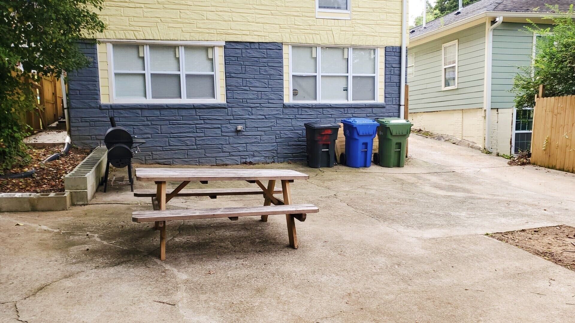 A backyard with a picnic table, a barbecue grill, and trash bins.