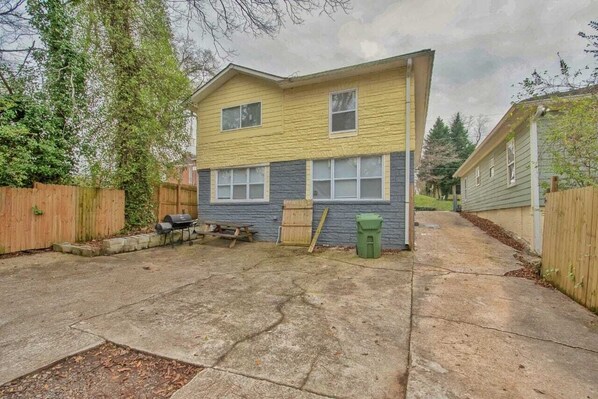 A two-story house with a front yard, a wooden fence, and a green trash bin.