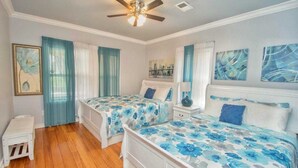 Ein Schlafzimmer mit zwei Betten, einem Deckenventilator, einer kleinen weißen Bank und Bildern an den Wänden.