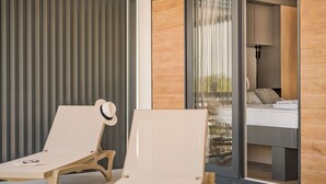 Een moderne kamer met een glazen deur naar een balkon, een bed met uitzicht en twee comfortabele fauteuils.