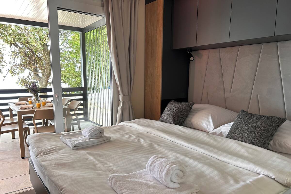 Un dormitorio moderno con una cama grande, dos almohadas y una toalla blanca bien doblada.
