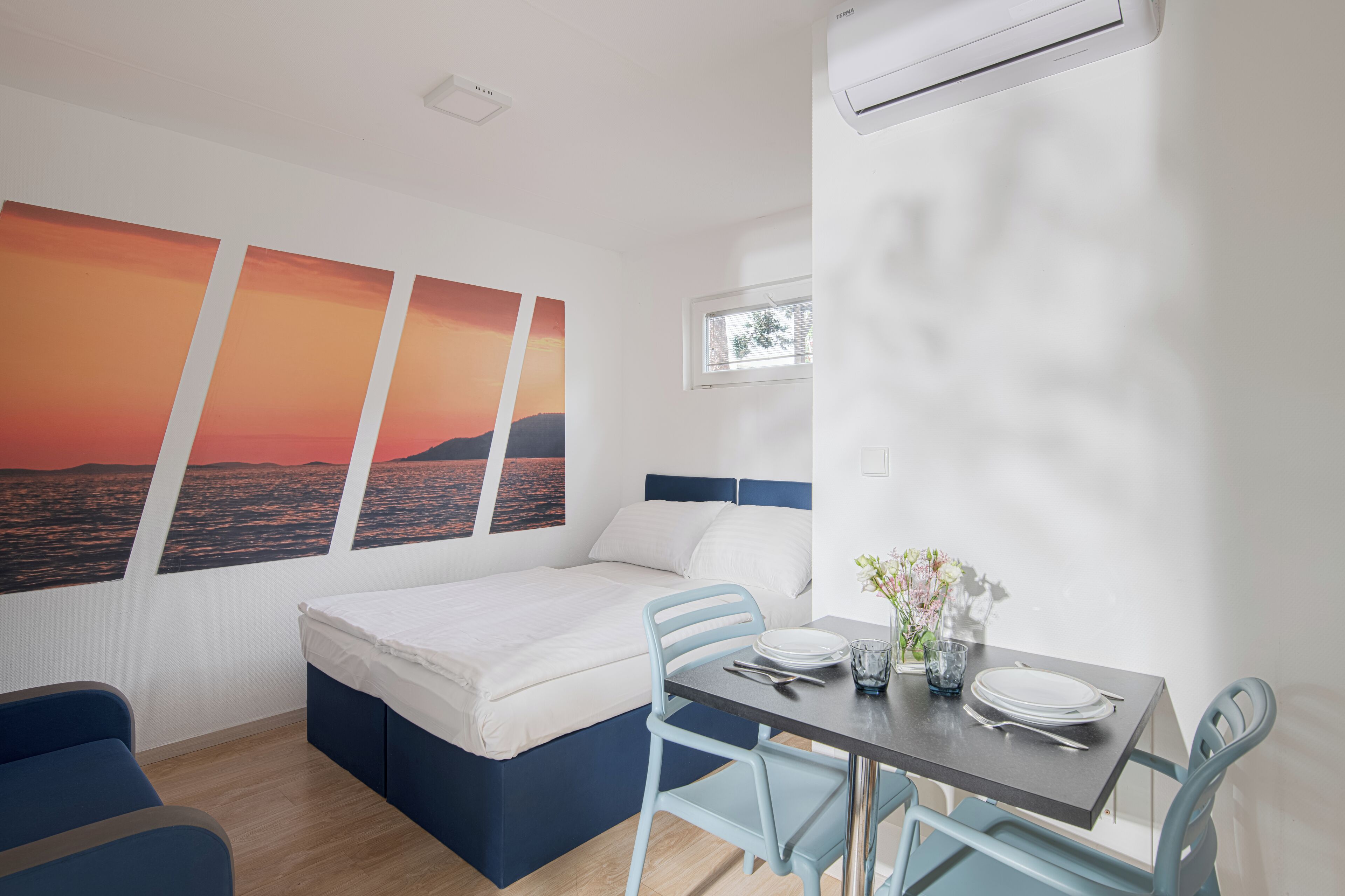 Una habitación moderna con cama, una mesa de comedor con sillas y una ventana con vista al mar.