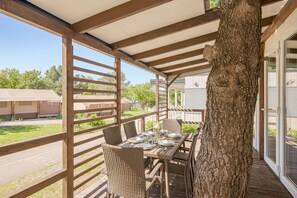 Un espace extérieur abrité, aménagé pour les repas, avec une table et des chaises en bois, un grand tronc d’arbre et une vue sur les environs.